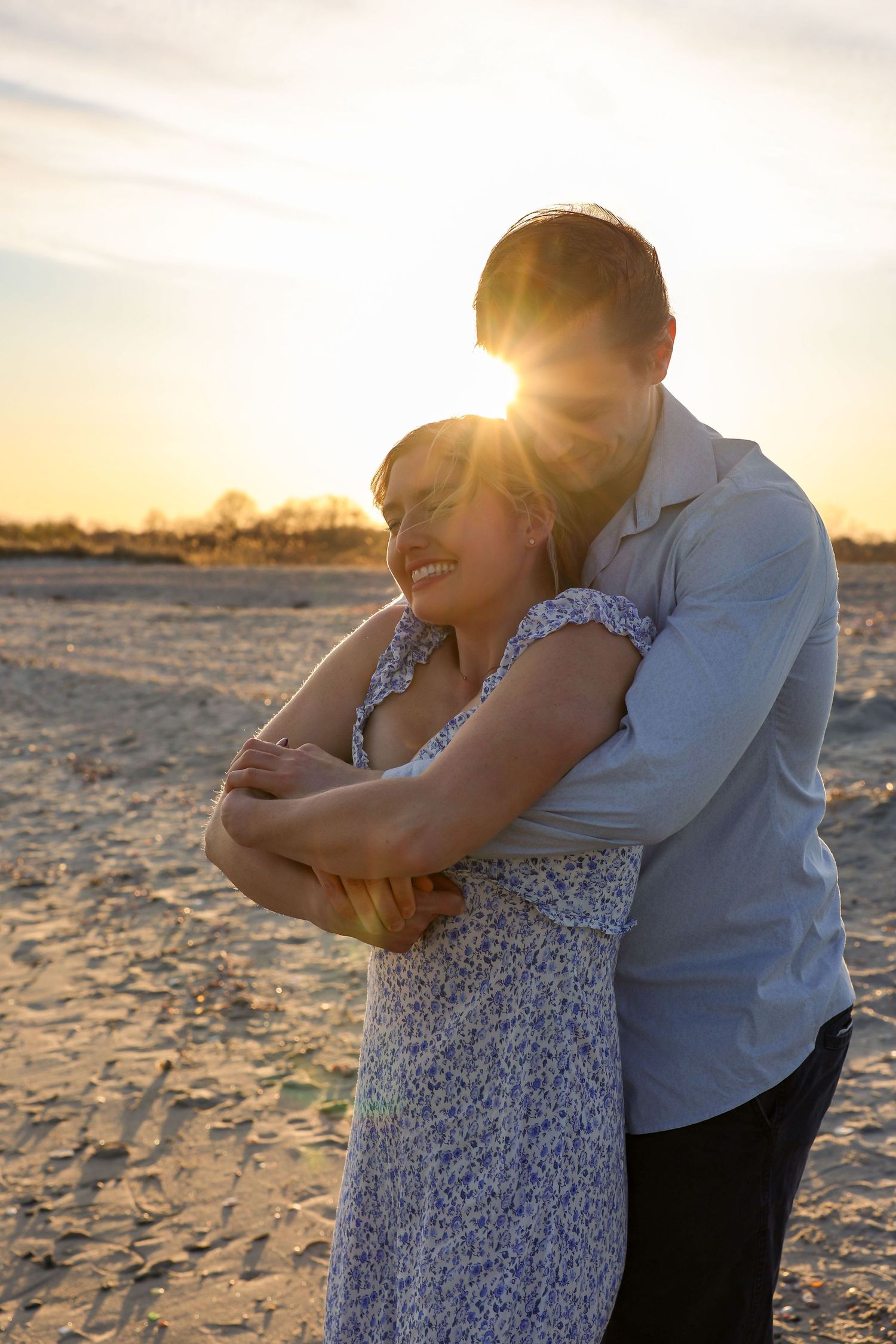 Couple embracing on beach with bright golden sunset sunburst glowing behind them.