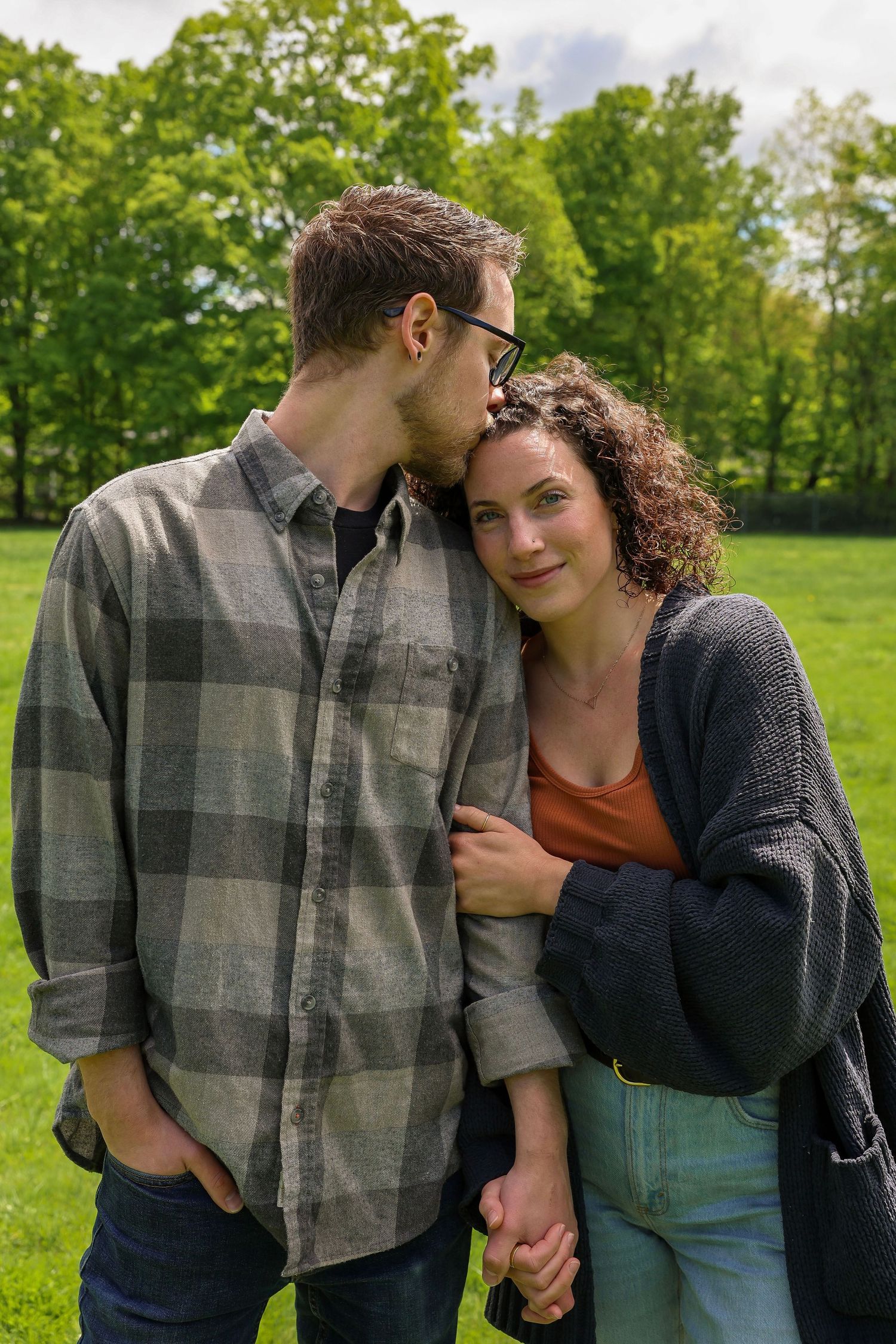 A loving couple standing close together as the man kisses the womans forehead in a green field.