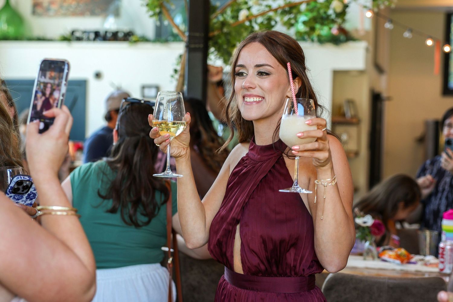 Smiling woman in burgundy dress holding white wine glass at an elegant birthday celebration.