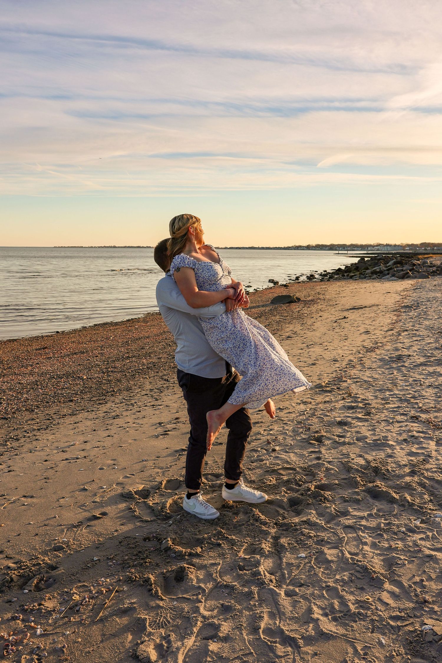 Man lifting woman in his arms on a sandy beach during a beautiful sunset.