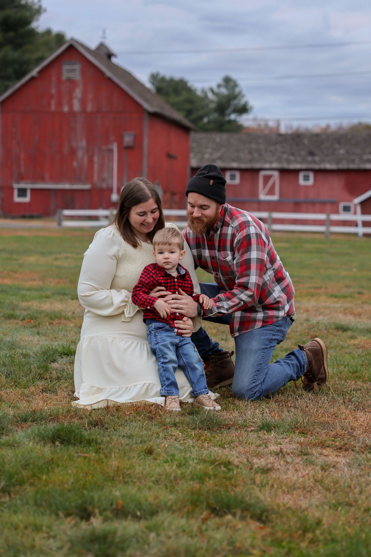 Parents interact playfully with baby during candid fall family photo session near red barn.