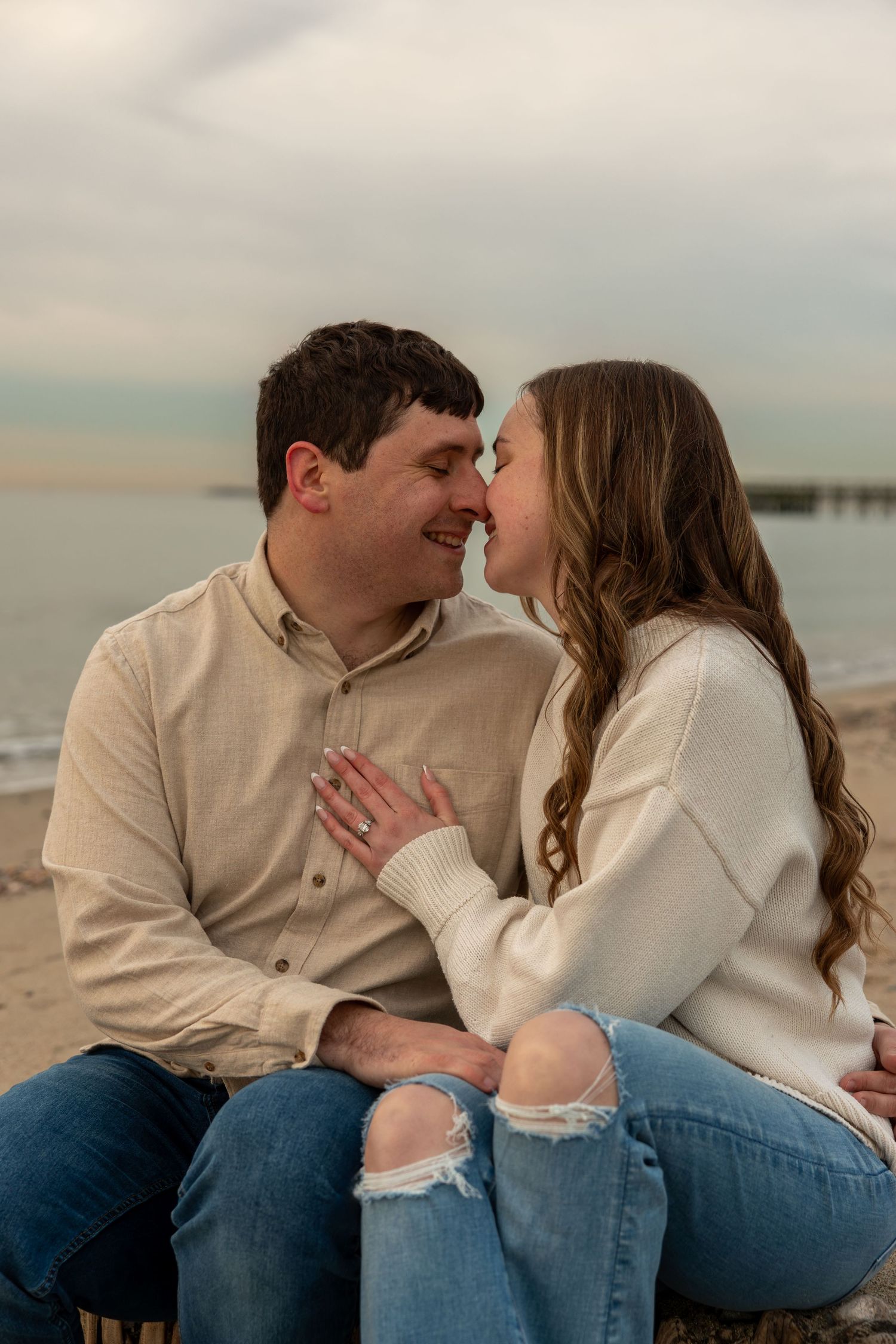 Couple sitting close together smiling at beach during stunning golden sunset.