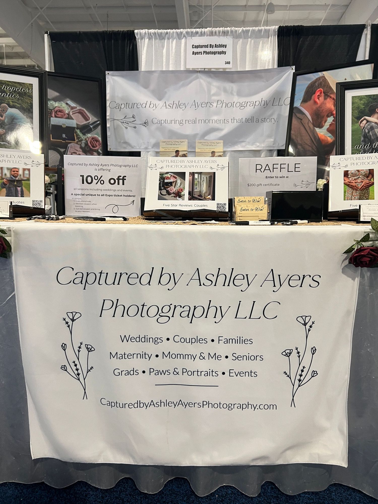 Captured by Ashley Ayers Photography LLC booth displaying wedding, family, and portrait services with a 10% off sign.