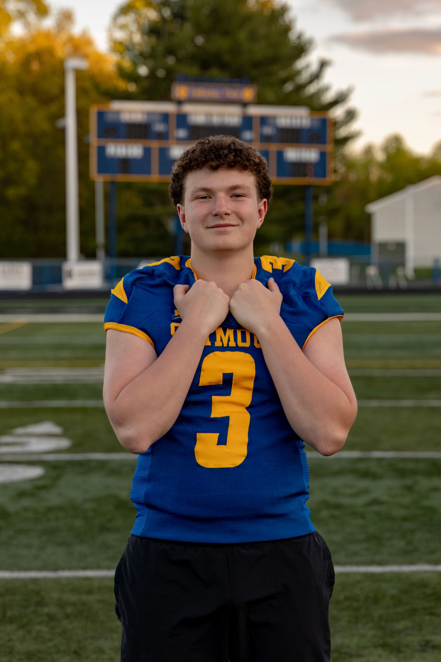 Seymour #3 football player smiling and grabbing jersey collar on field at golden hour.