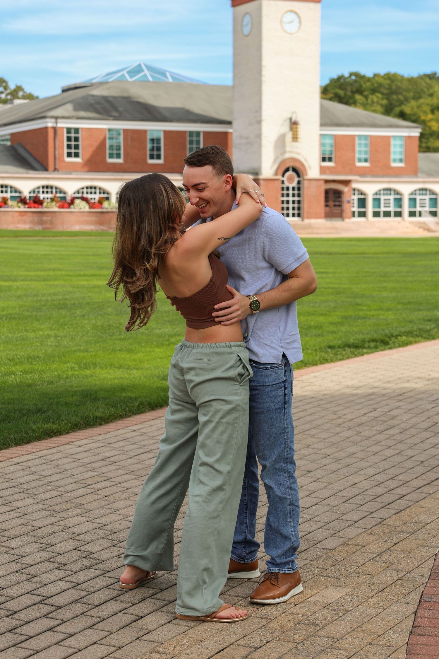 Couple sharing a romantic embrace and kiss on a brick pathway in front of a brick campus building.
