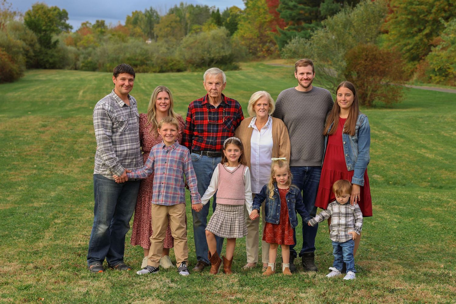 Extended multigenerational family group portrait outdoors with colorful fall foliage background.