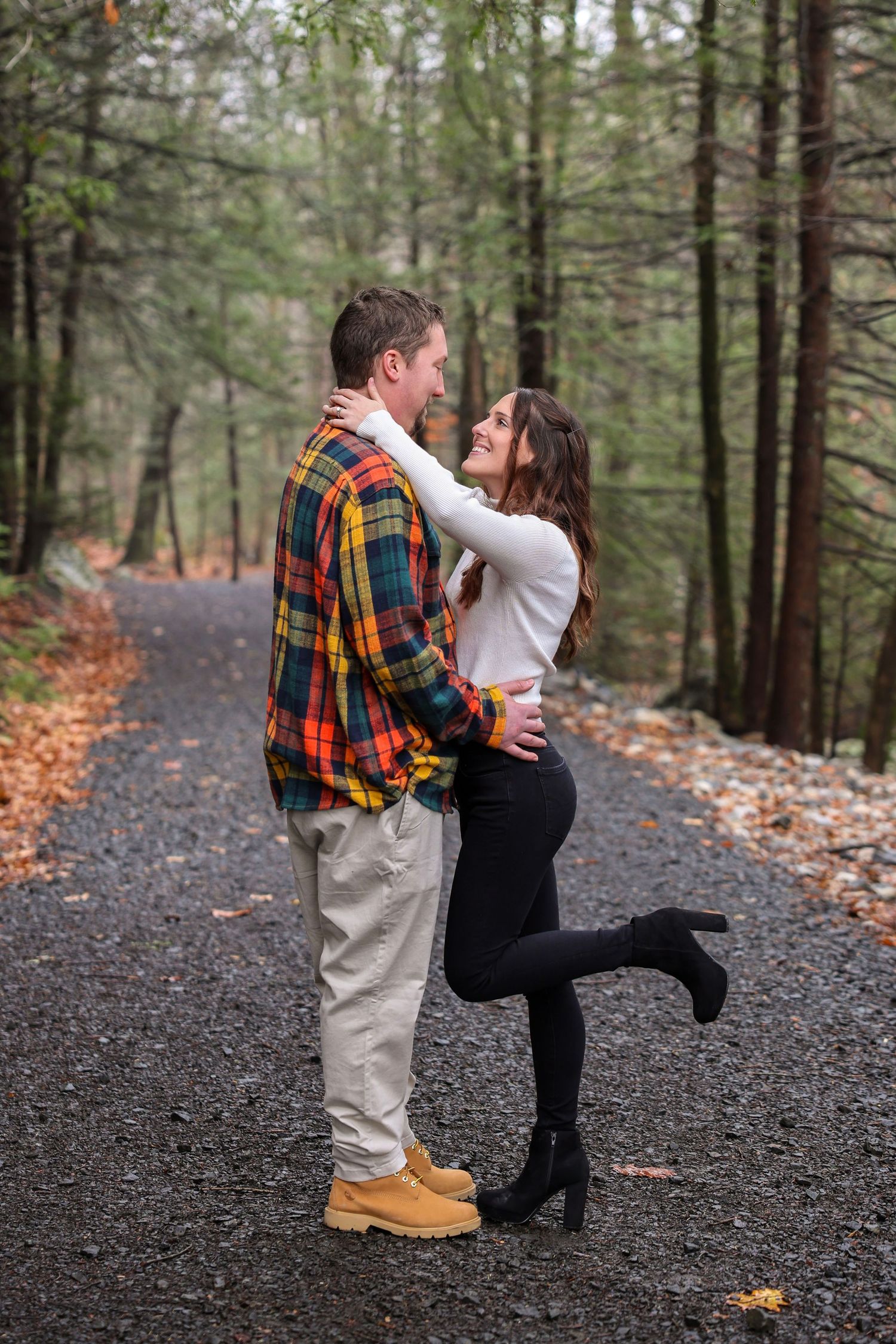 Couple embracing and smiling at each other on a forest path in autumn, man in plaid shirt and woman in white top.