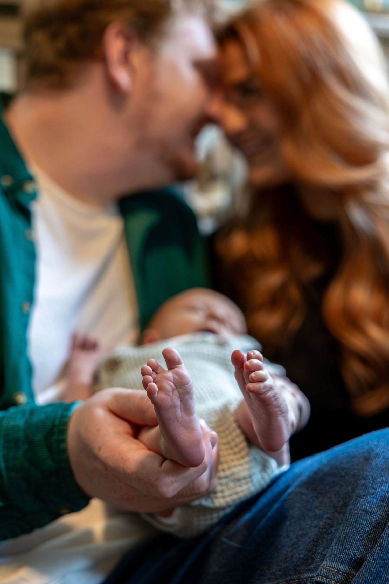Close-up of newborn baby feet held by parents smiling together in a warm, tender family moment.