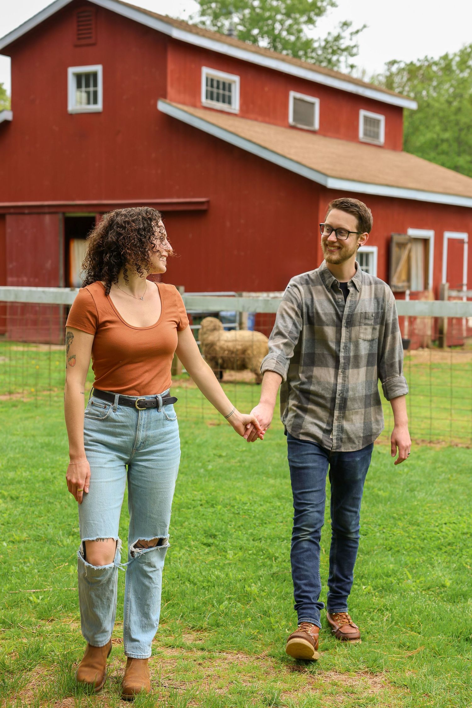 A happy couple holding hands and walking together in front of a classic red barn on a farm.