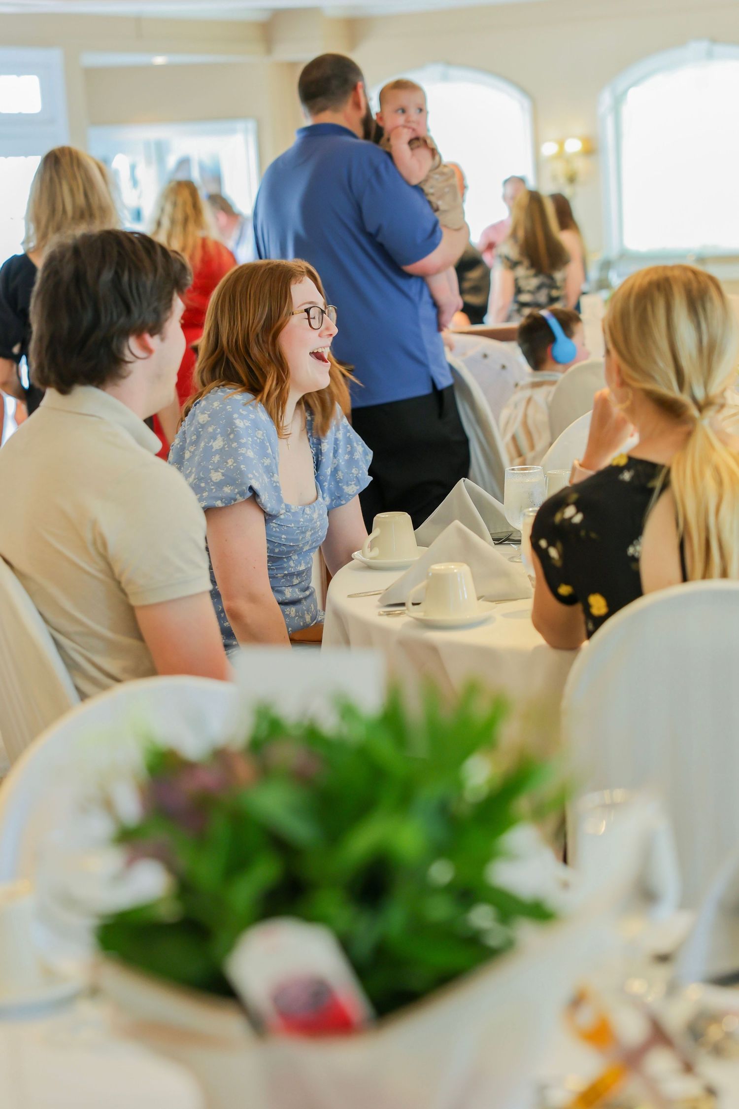 Young redhead woman laughing with friends at an elegant indoor party reception dinner table.