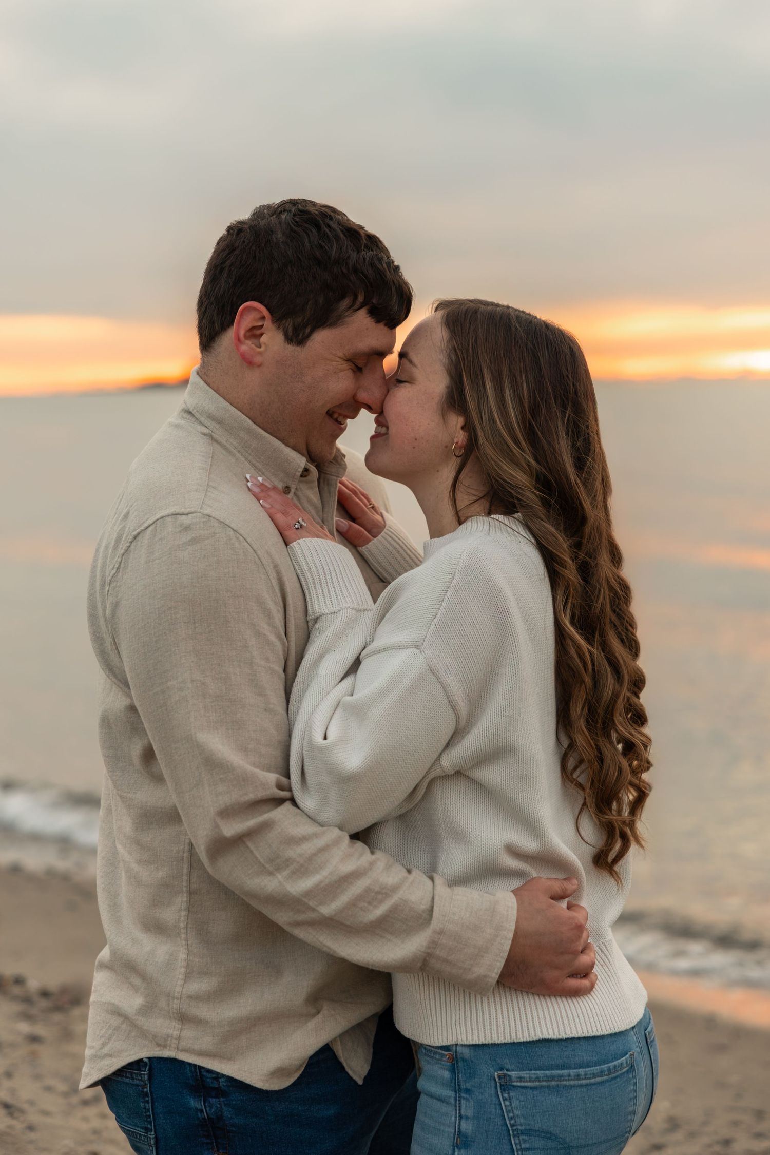 Romantic couple embracing and touching noses at beach during vibrant orange sunset.