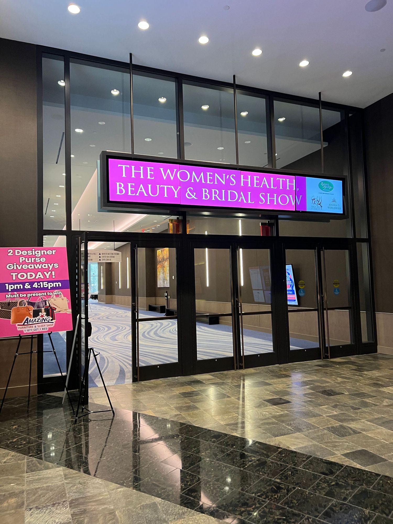 The entrance to The Women's Health Beauty and Bridal Show with illuminated pink signage above glass doors in a convention center.