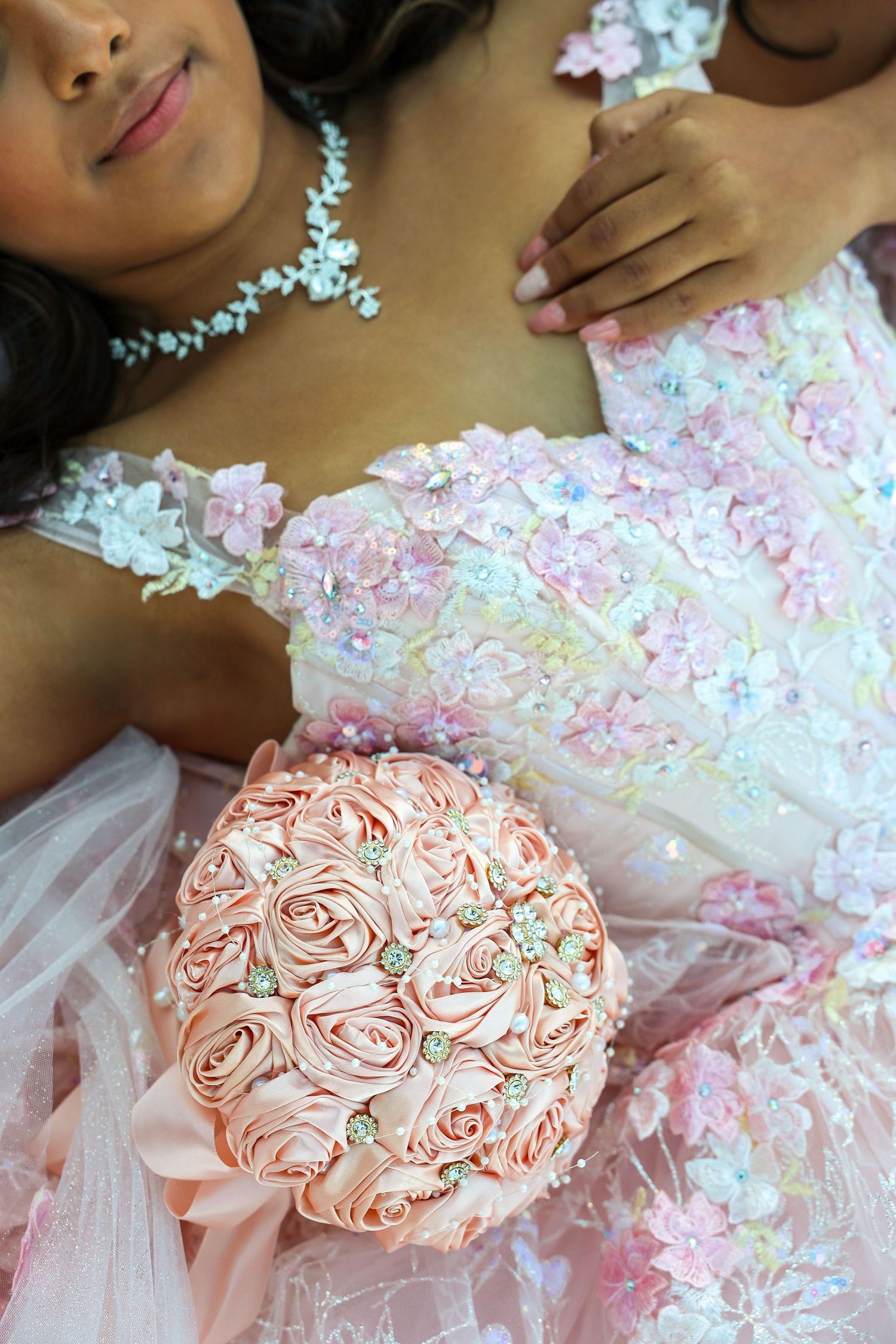Close-up of quinceañera girl in pink floral lace gown holding an elegant pink satin rose bouquet.