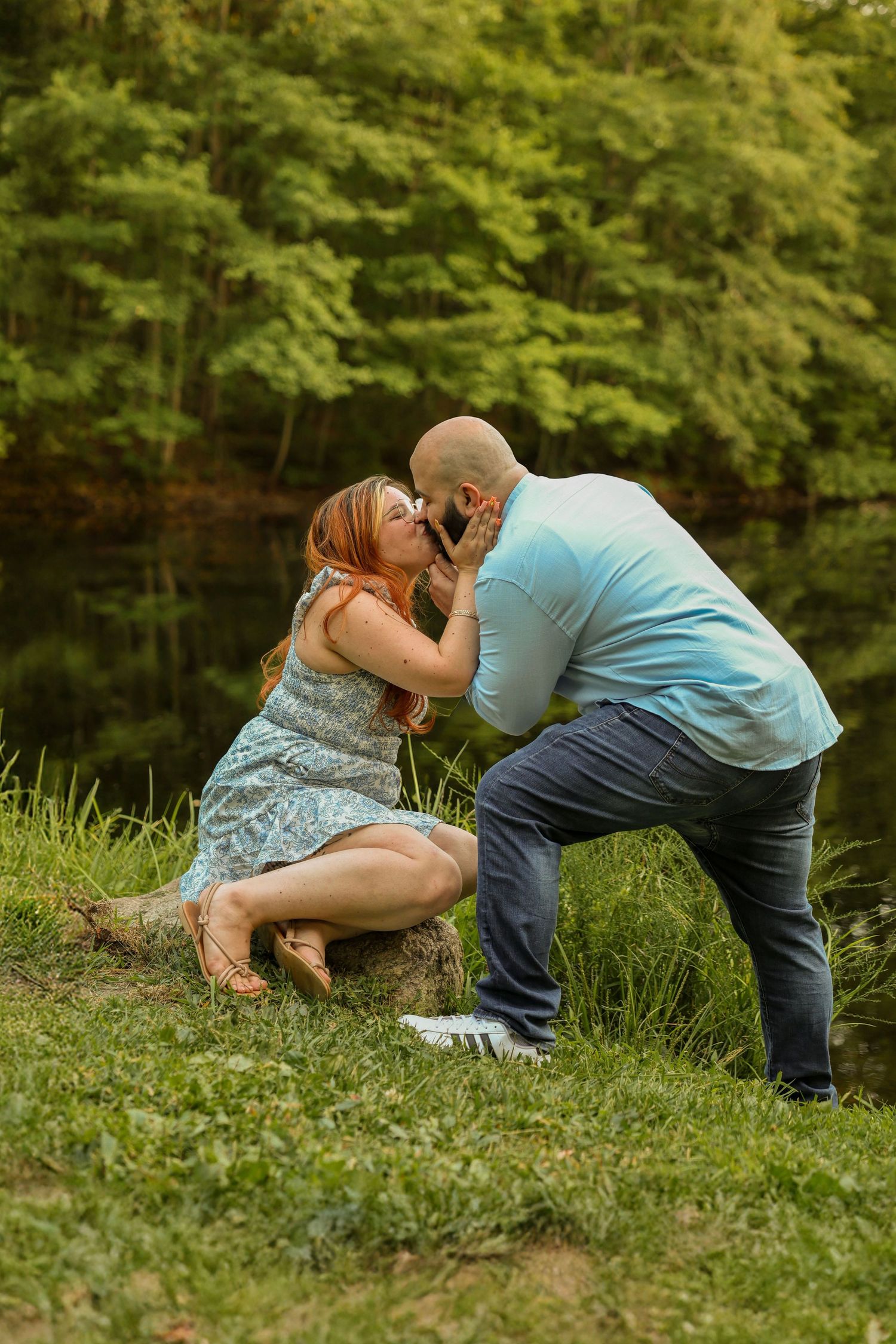 Couple sharing a tender kiss near a peaceful forest lake during a romantic outdoor engagement session.