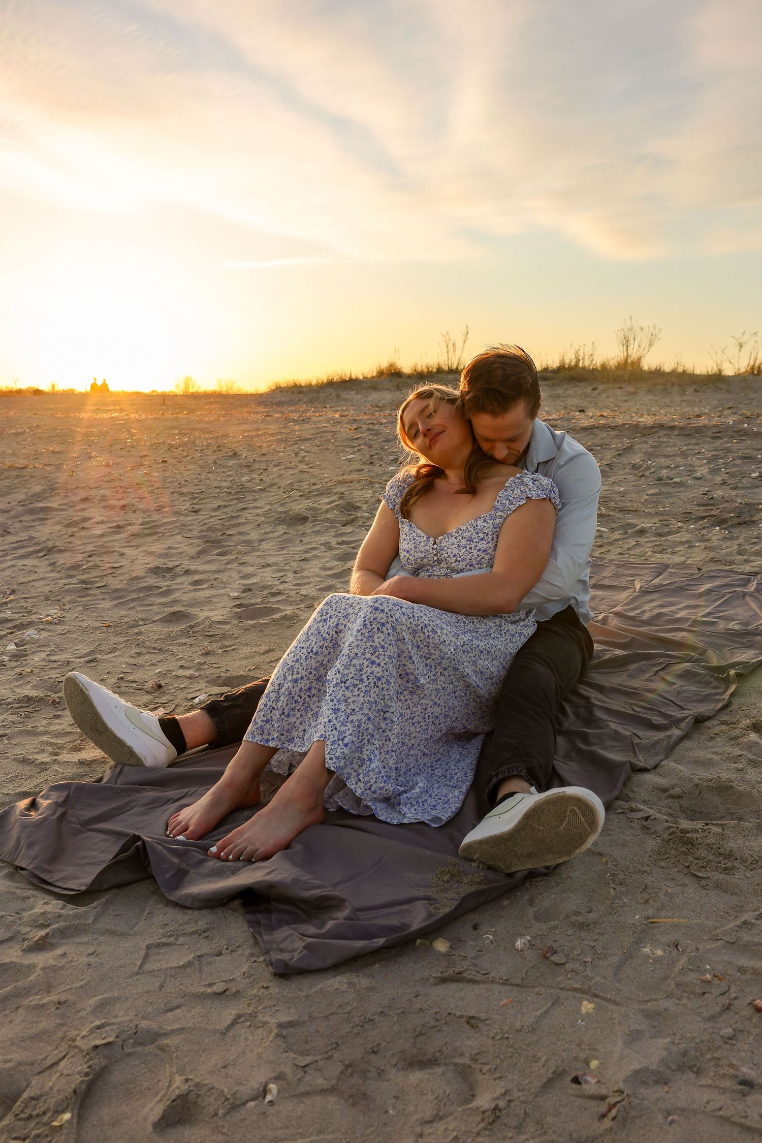 Couple sharing a romantic sunset moment on a sandy beach, sitting on a blanket in a warm golden glow.