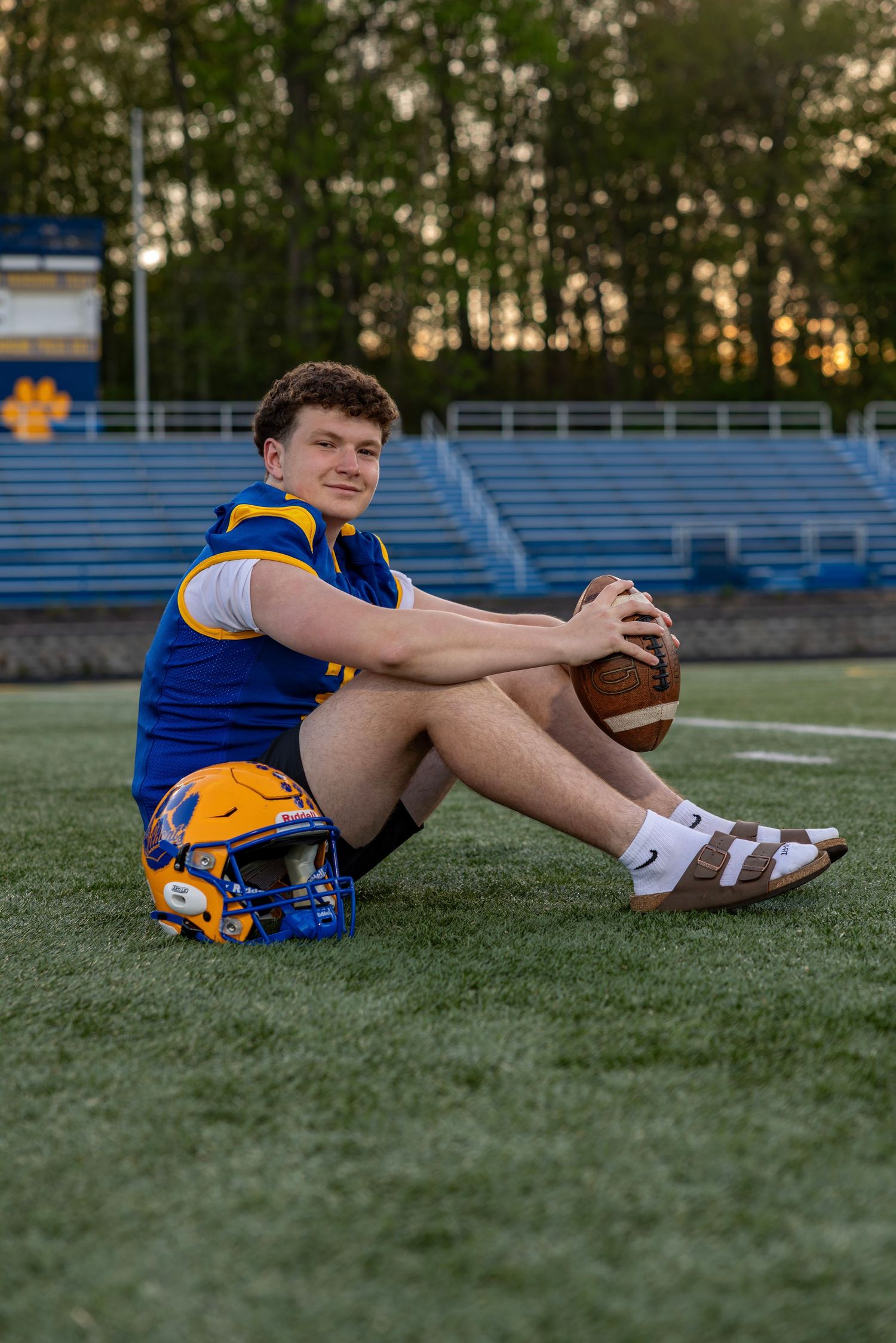 Seymour #3 football player sitting on field leaning on blue helmet holding football at golden hour.