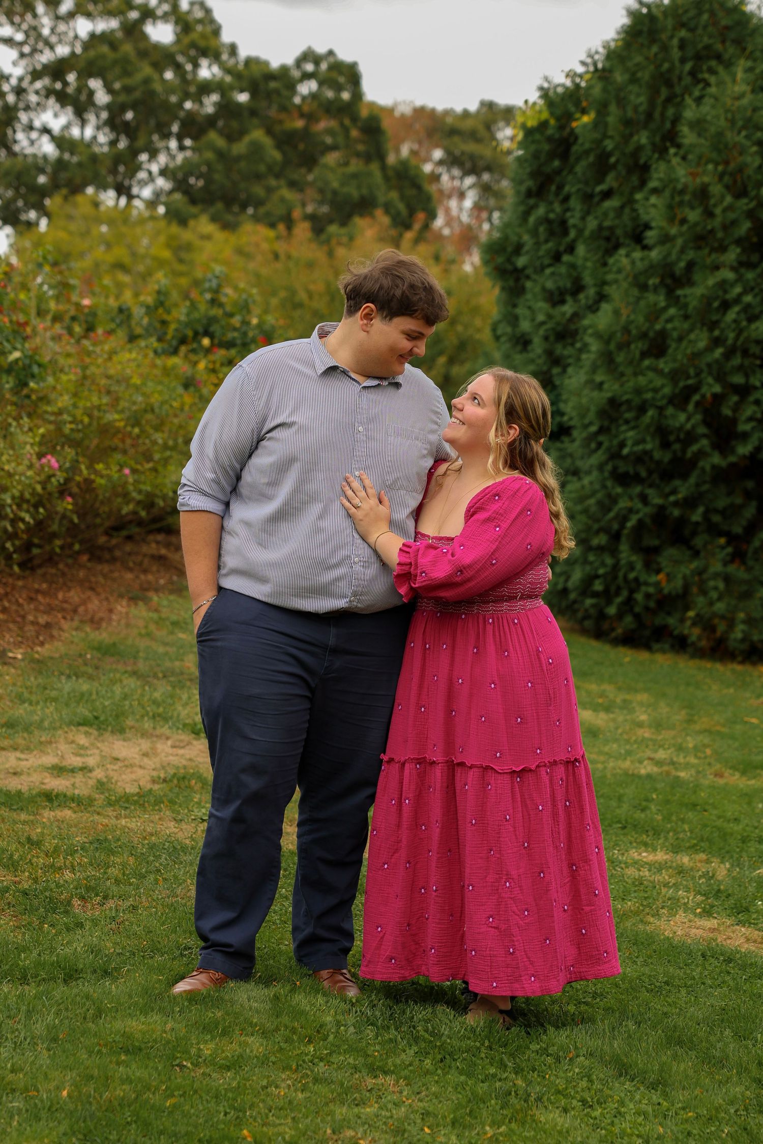 Couple gazing at each other lovingly in lush garden, woman in pink dress, man in blue shirt.