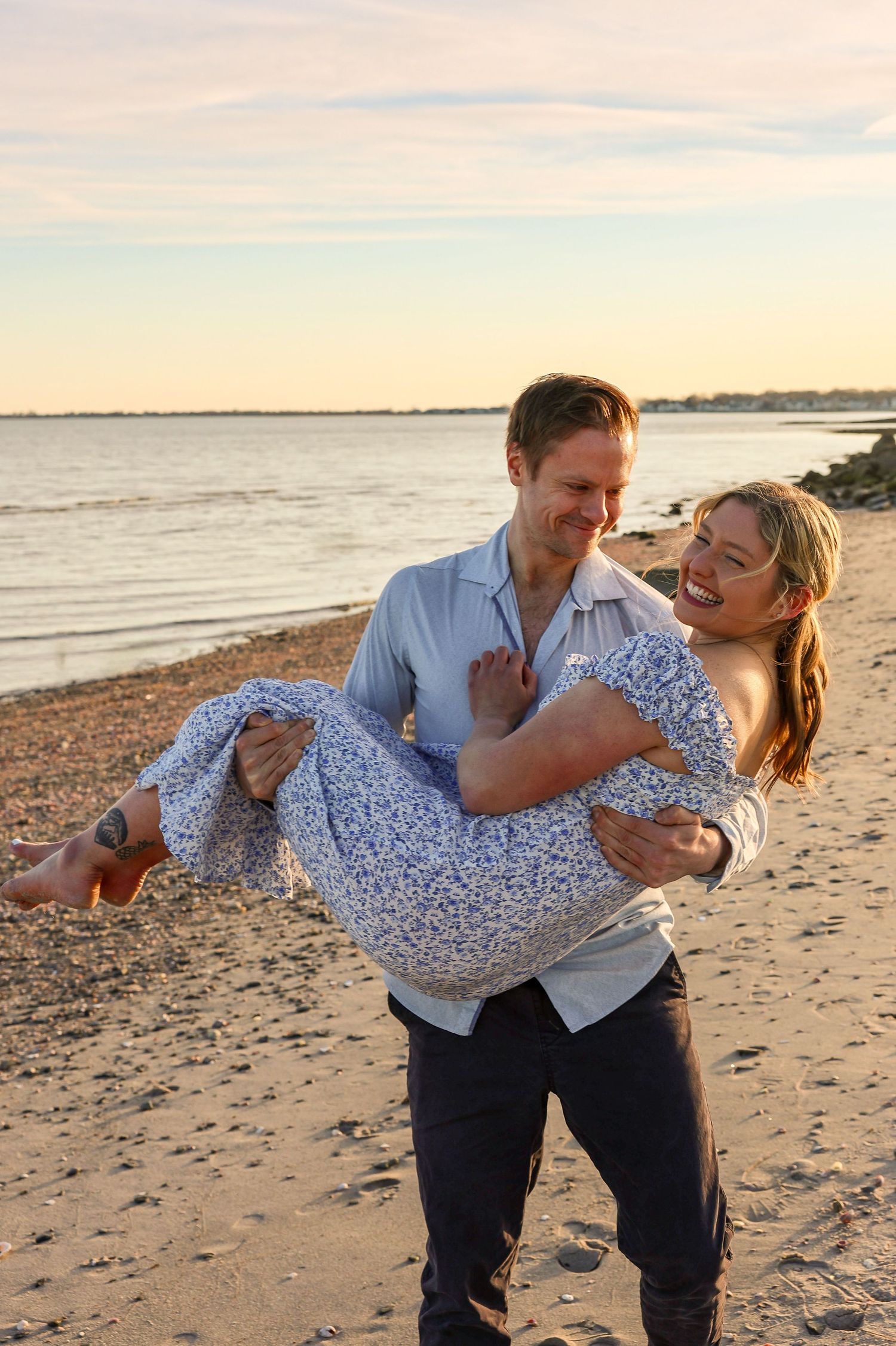 Man carrying laughing woman in his arms on a sunny beach at golden hour.