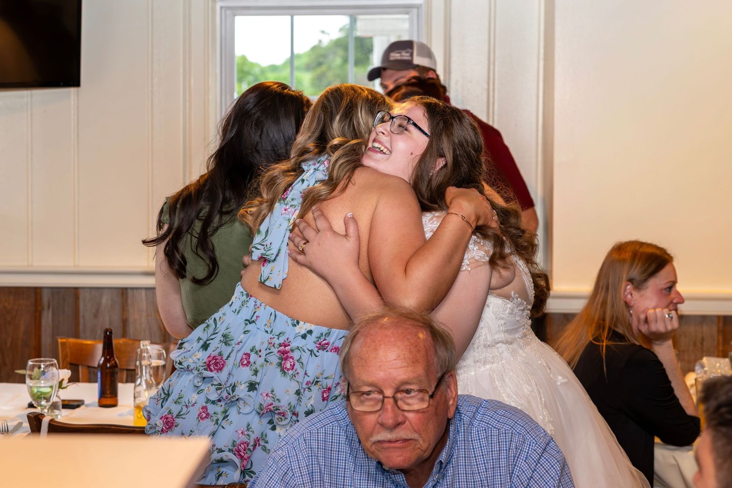 Bride receives warm group hug from friends and family at wedding reception dinner.