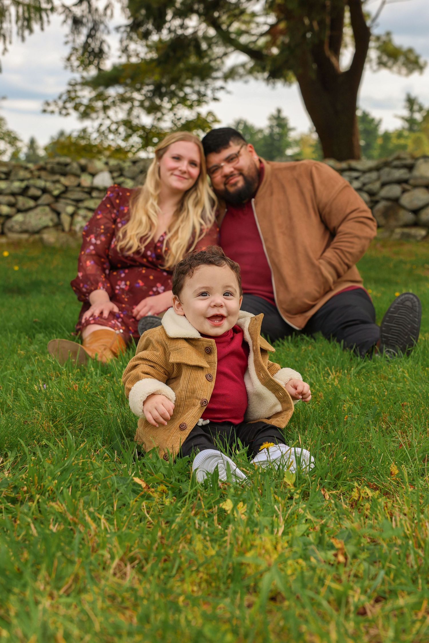 Young family with an adorable baby boy sitting on grass in an autumn park setting.