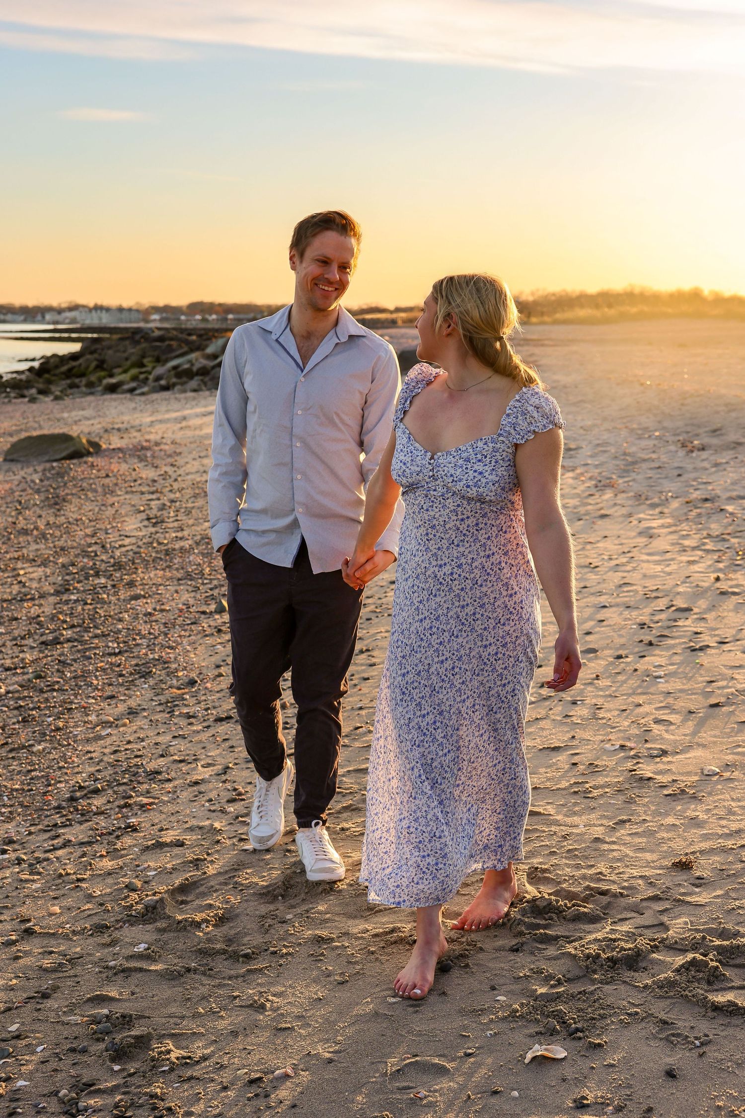 Couple walking hand in hand on sandy beach during warm golden sunset together.