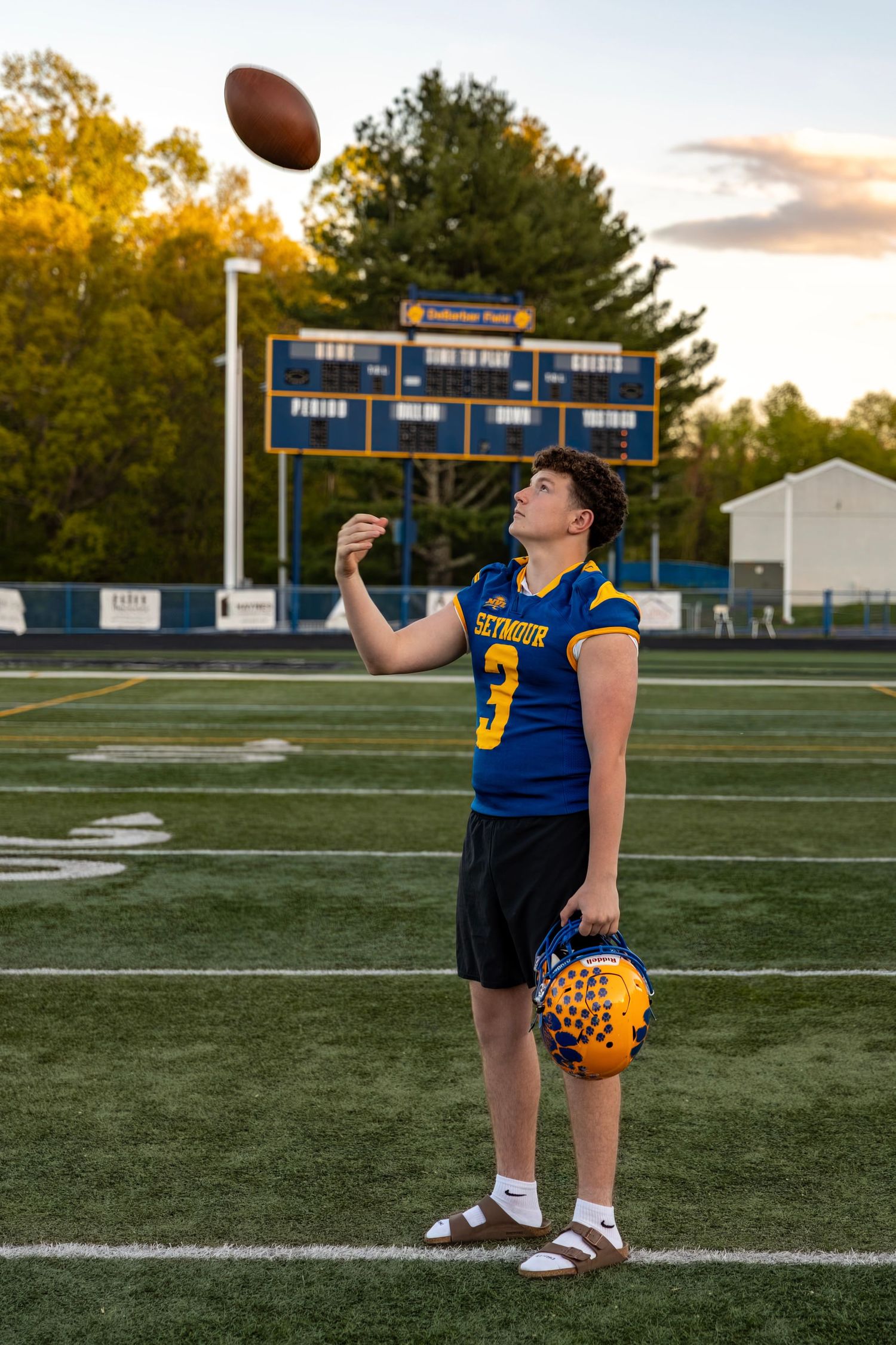 Seymour #3 football player tossing ball in air at sunset with scoreboard visible in background.