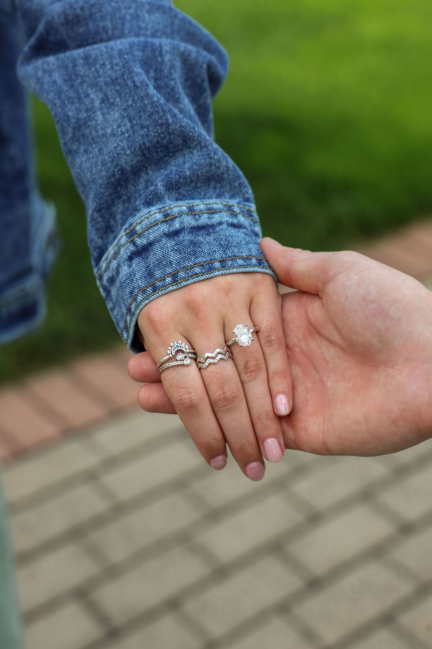 Close-up of a woman's hand wearing a diamond engagement ring held by her partner outdoors.