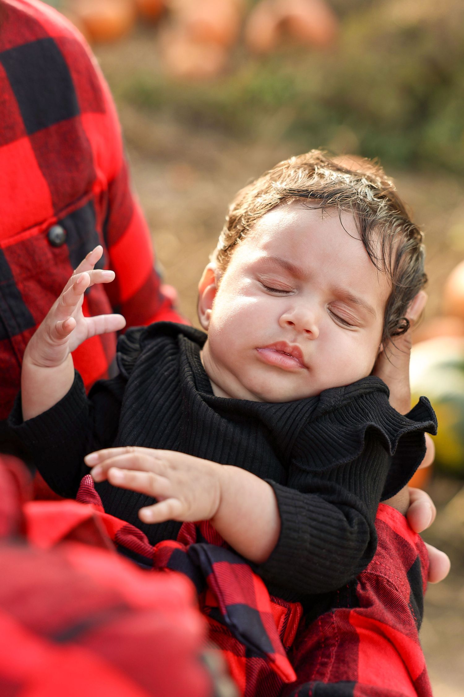 Peaceful sleeping newborn baby in black outfit cradled in arms of parent wearing red plaid flannel shirt.