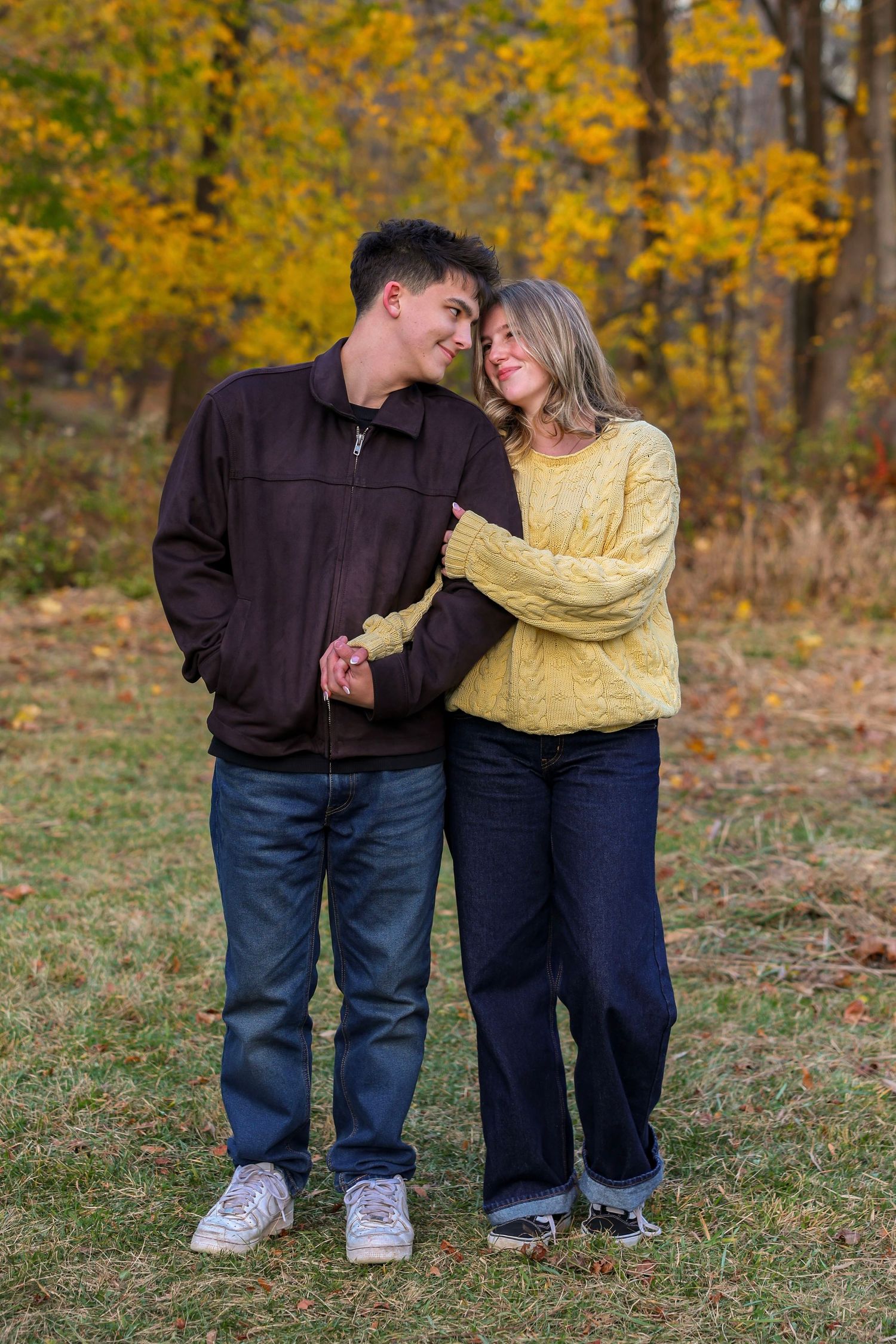 Happy young couple holding hands and smiling at each other in autumn park setting.