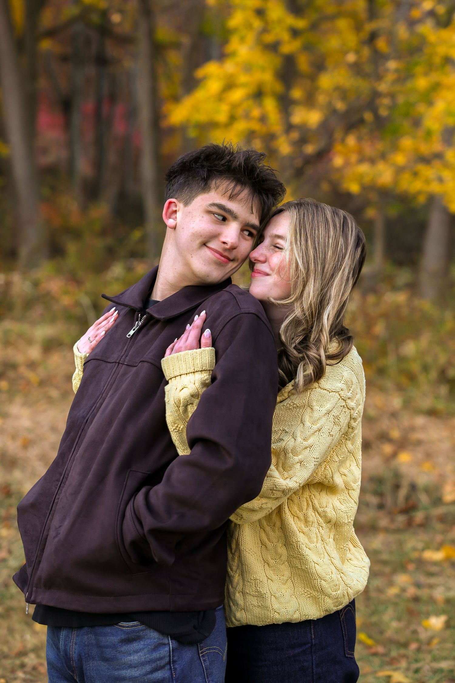 Young woman hugging man from behind smiling in golden autumn forest setting.