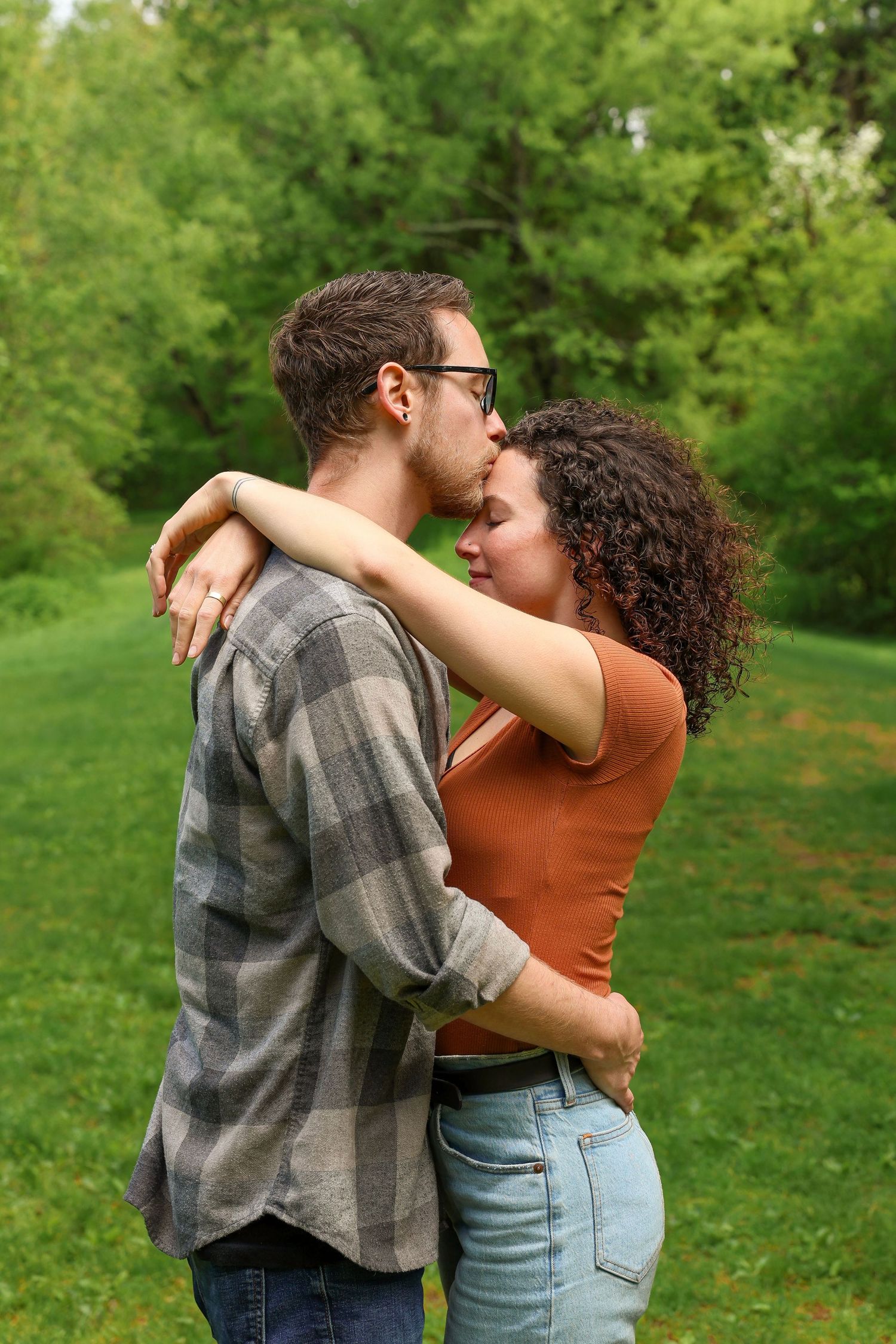A romantic couple embracing and kissing outdoors in a lush green park setting during spring.