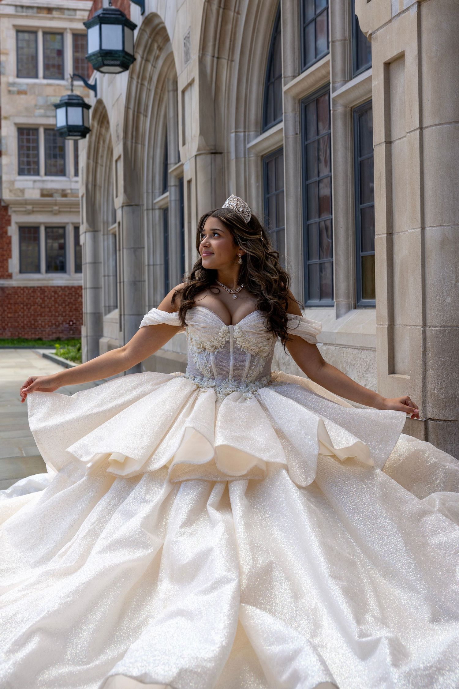 Young woman in stunning white quinceañera ball gown spreading skirt at gothic building.