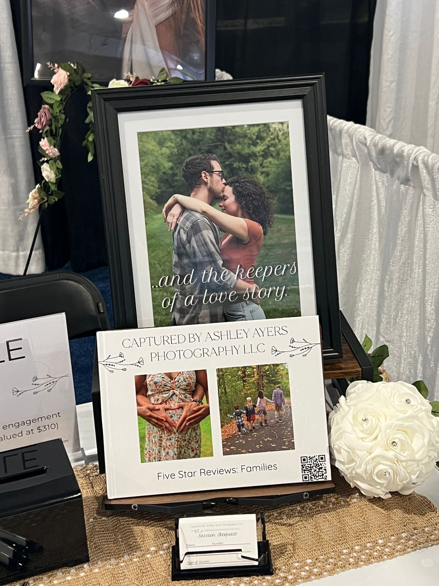 A framed romantic couple photo display for Captured by Ashley Ayers Photography LLC with five-star family reviews at a bridal expo booth.