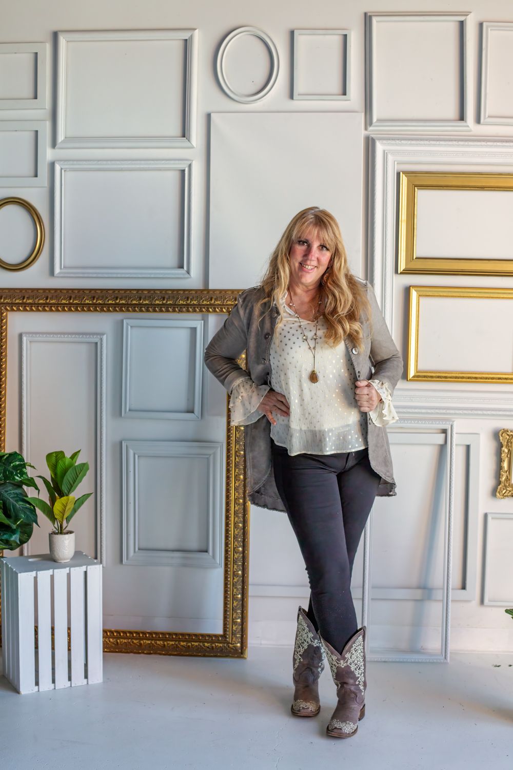 Person posing against decorative wall with empty frames in grey and gold tones.