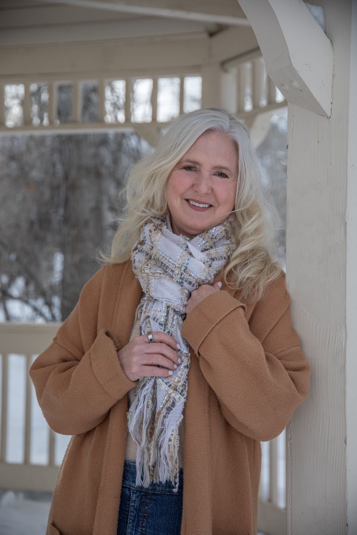 Winter portrait featuring tan coat and patterned scarf on snowy porch.