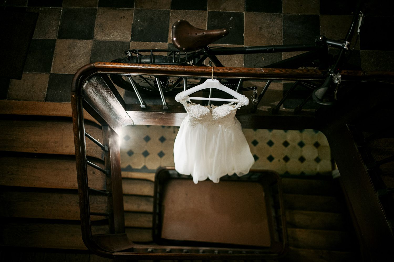 Delicate white flower girl dress hanging on a hanger over a vintage wooden staircase railing.