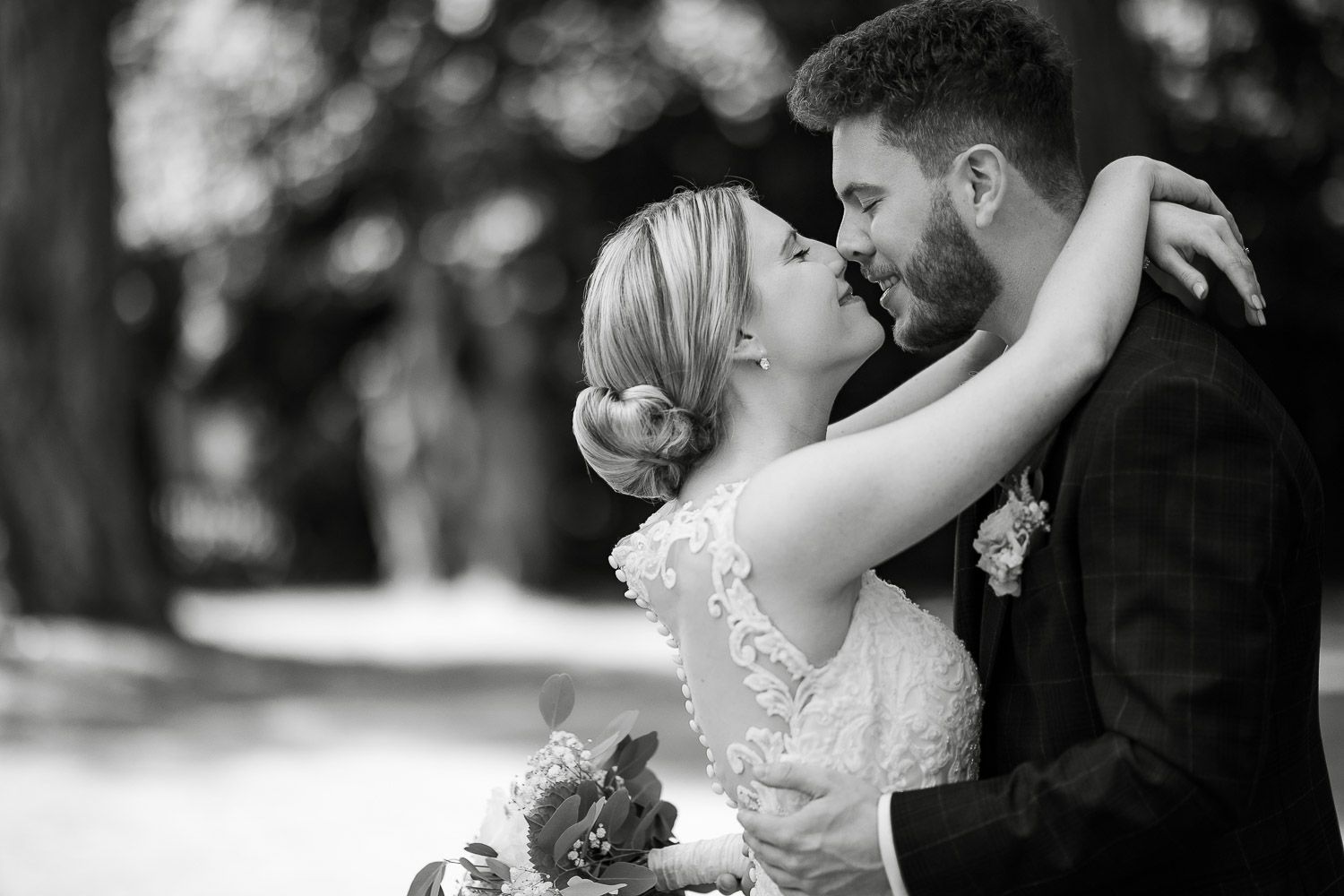 Black and white photo of bride and groom in a romantic embrace surrounded by trees.