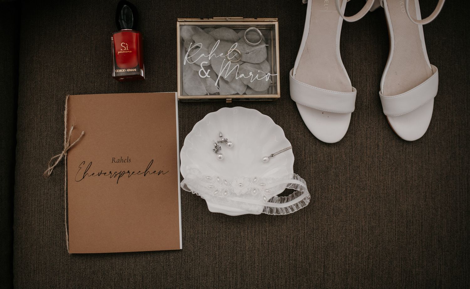 Flat lay of bridal accessories including white heels, ring dish, vows booklet, and nail polish.