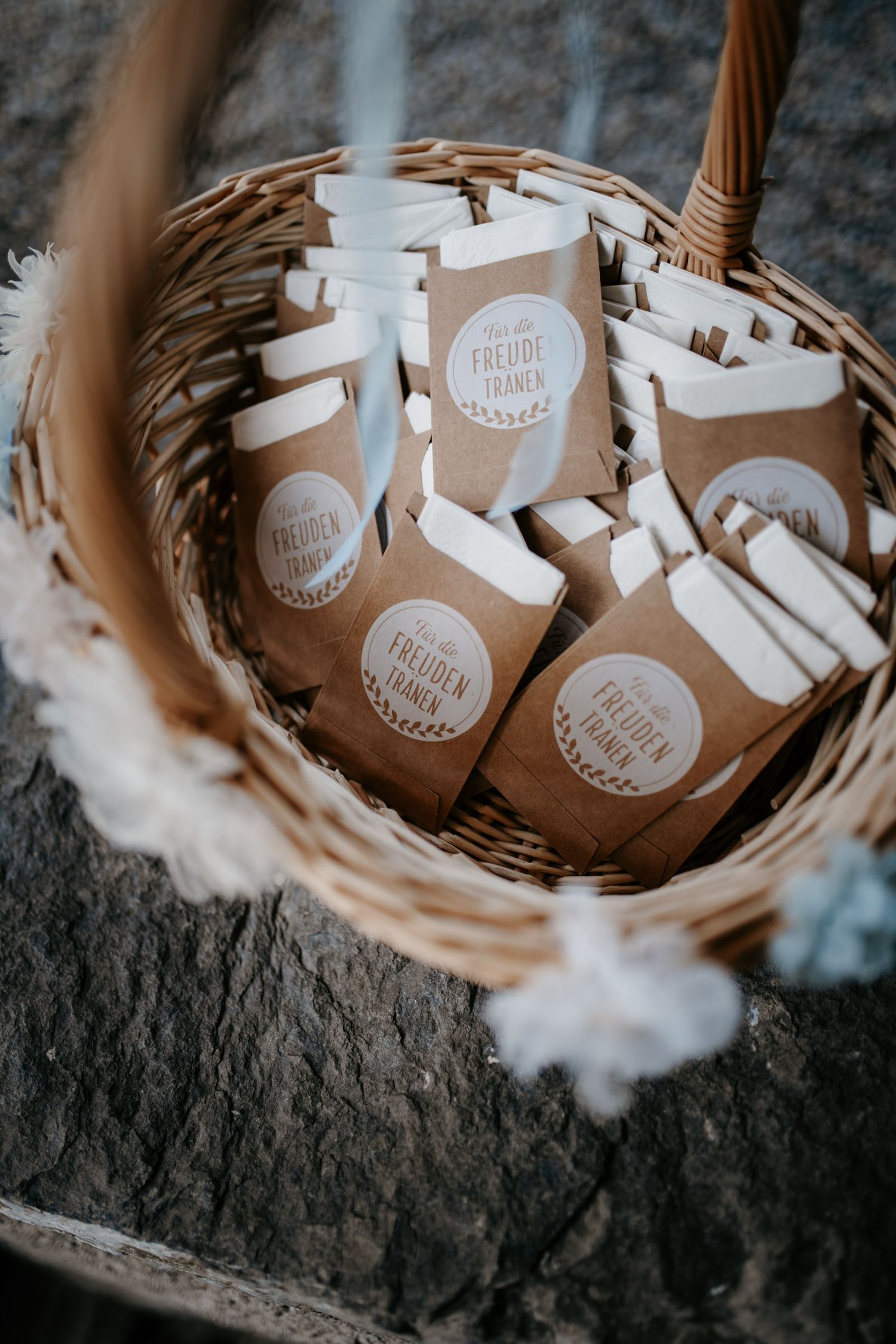 Wicker basket filled with kraft paper wedding favor bags labeled Freudentranen for guests.