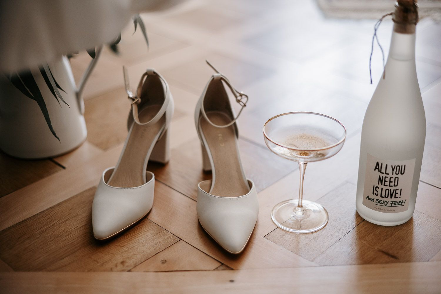 White bridal heels with ankle straps beside a martini glass and bottle reading All You Need Is Love.