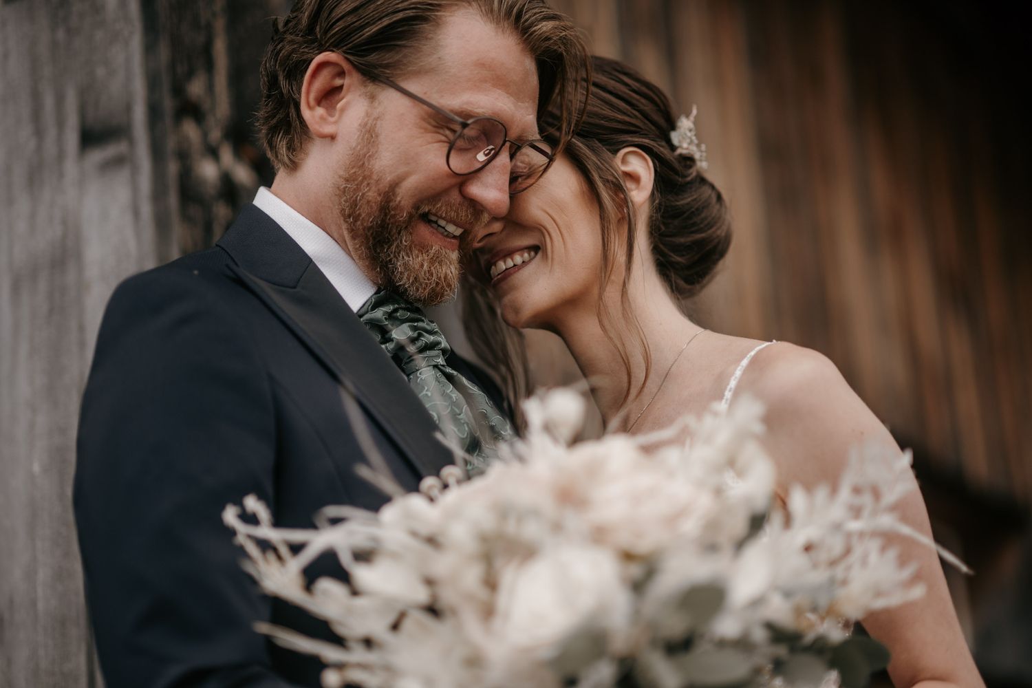 Bride and groom sharing an intimate moment smiling at each other with a white floral bouquet.
