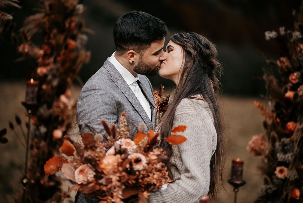 Couple sharing a romantic kiss surrounded by autumn floral arrangements and warm candlelight.