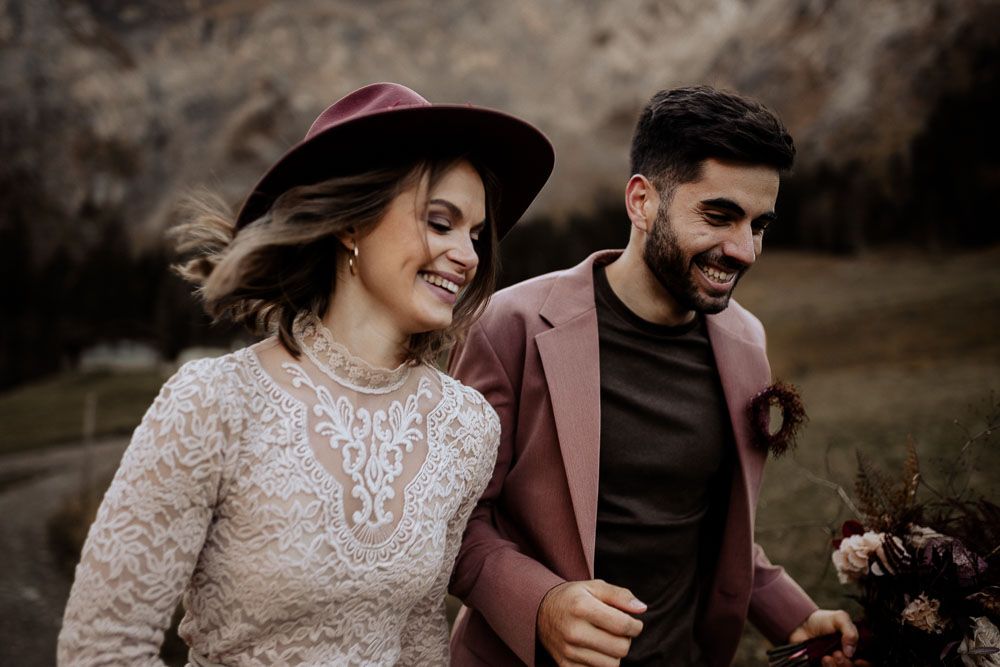 Stylish couple walking outdoors with bride in lace dress and groom in dusty rose blazer.