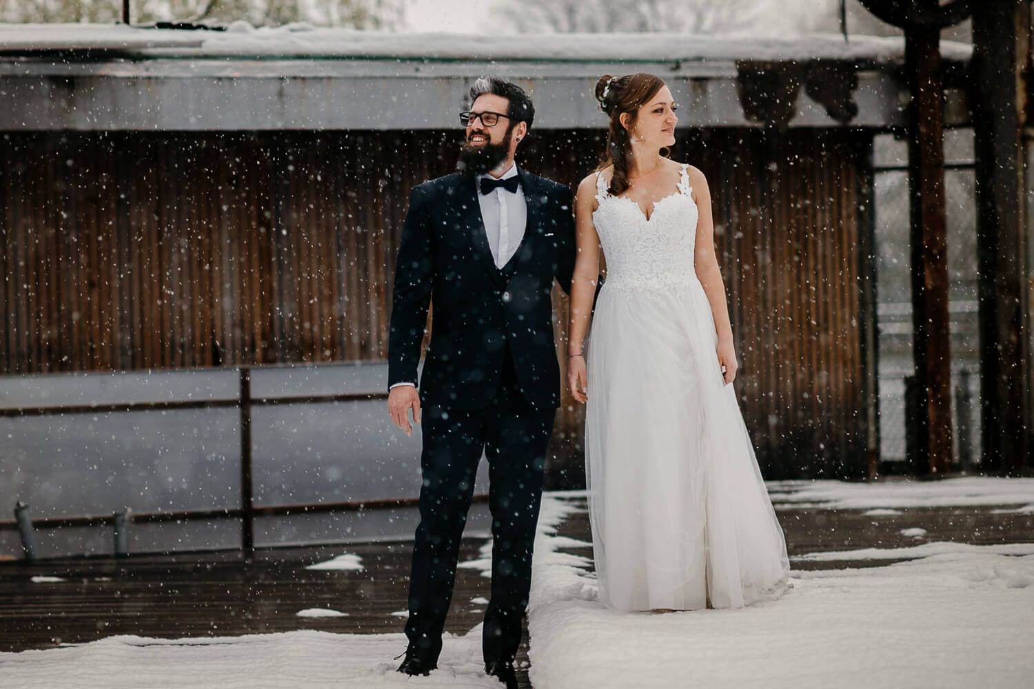 Elegant bride and groom standing in snowy winter landscape during romantic outdoor wedding portrait.