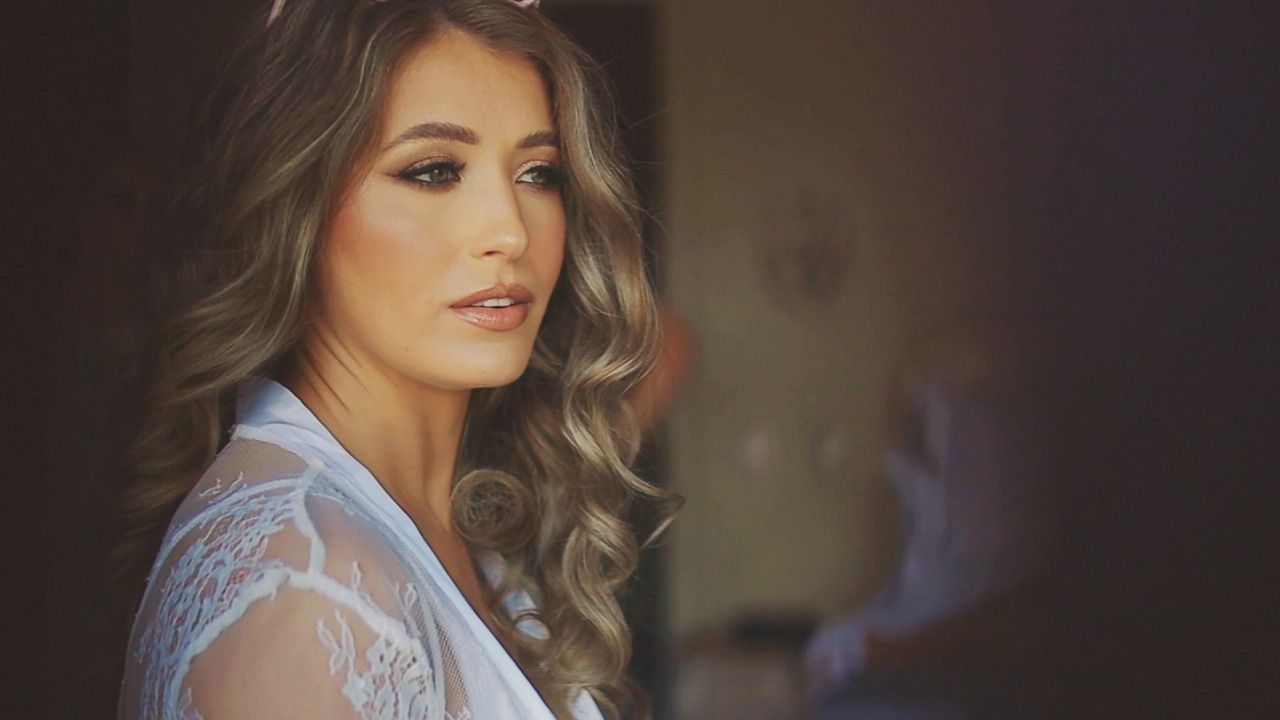 Beautiful bride in white lace robe with soft curls and elegant makeup before wedding.