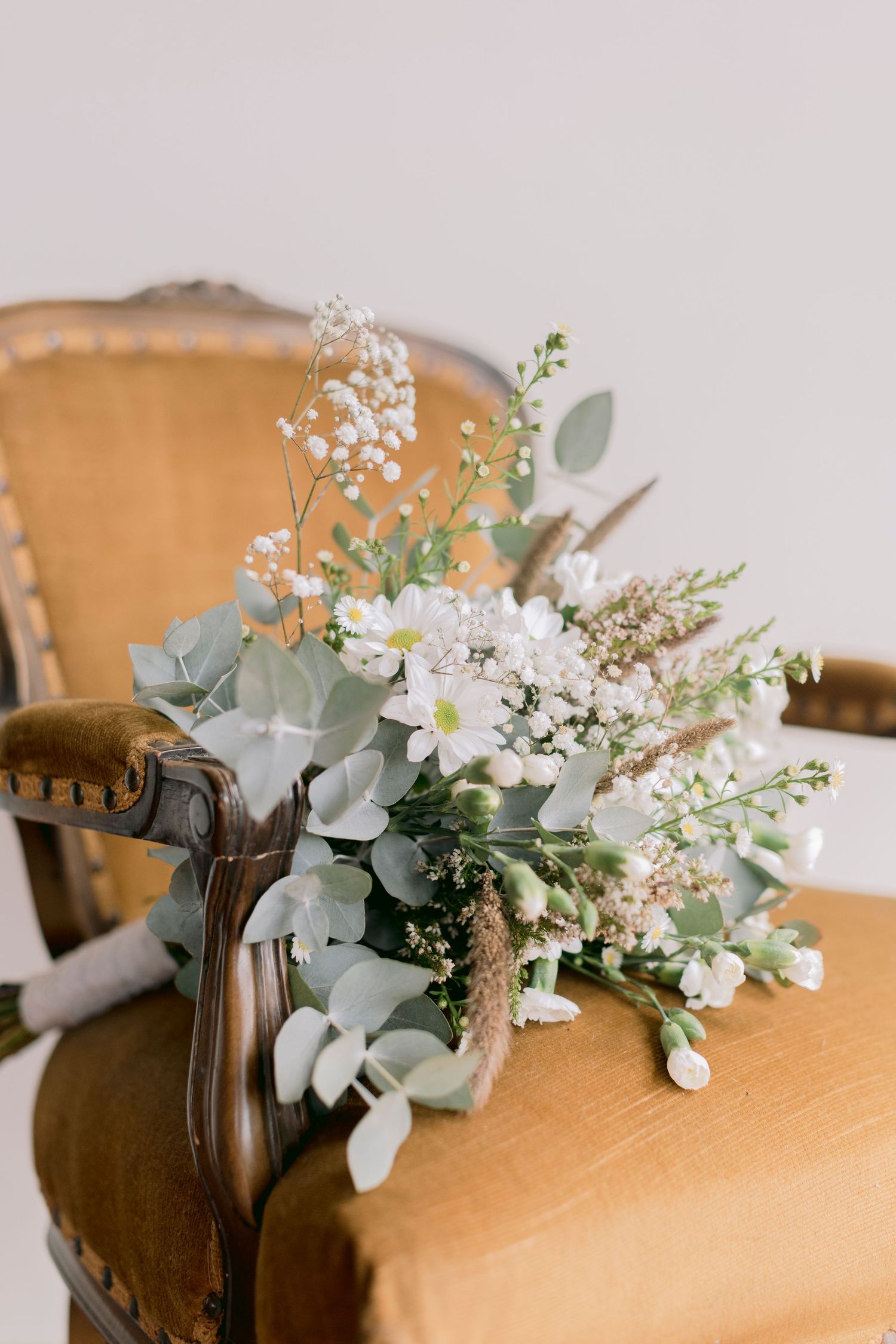 Romantic bridal bouquet with white blooms, eucalyptus leaves, and baby's breath on vintage chair.