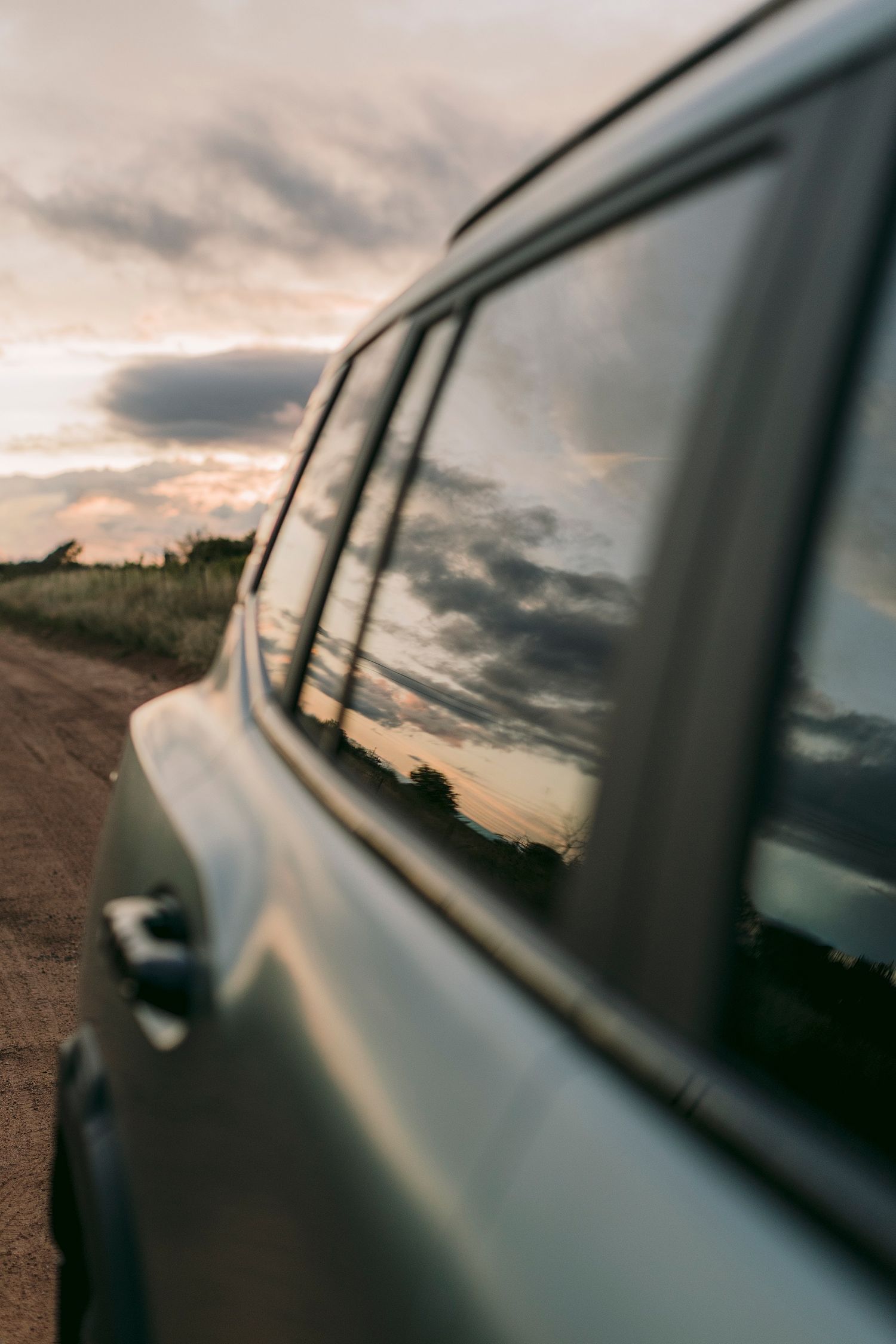 Jetour car parked on a dirt road at sunset, with dramatic clouds reflected in the side window.