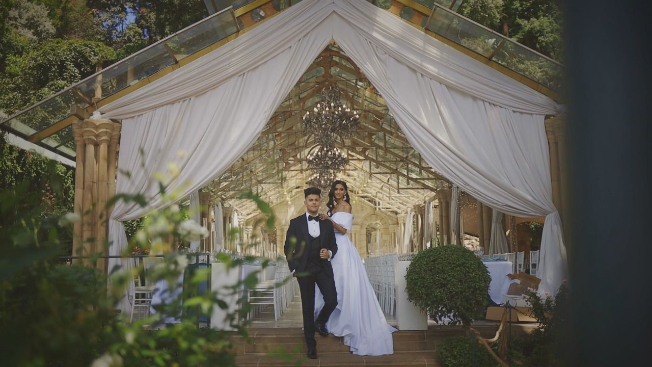 Elegant wedding couple standing under a draped white canopy at a romantic outdoor venue.