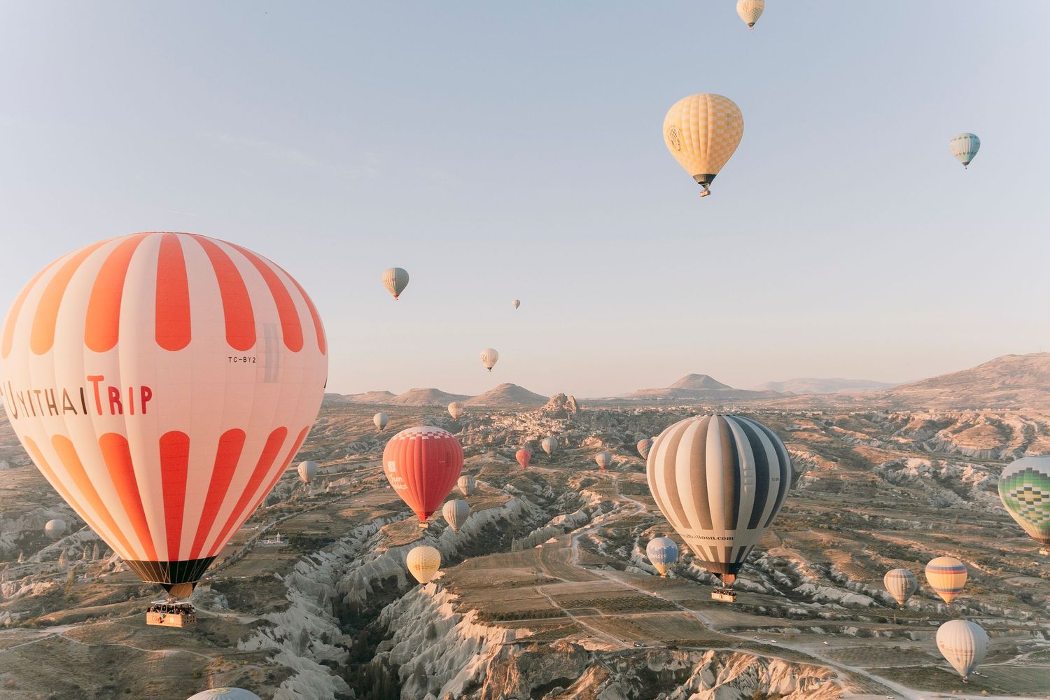 Colorful hot air balloons soaring over the rocky landscape of Cappadocia, Turkey at sunrise.
