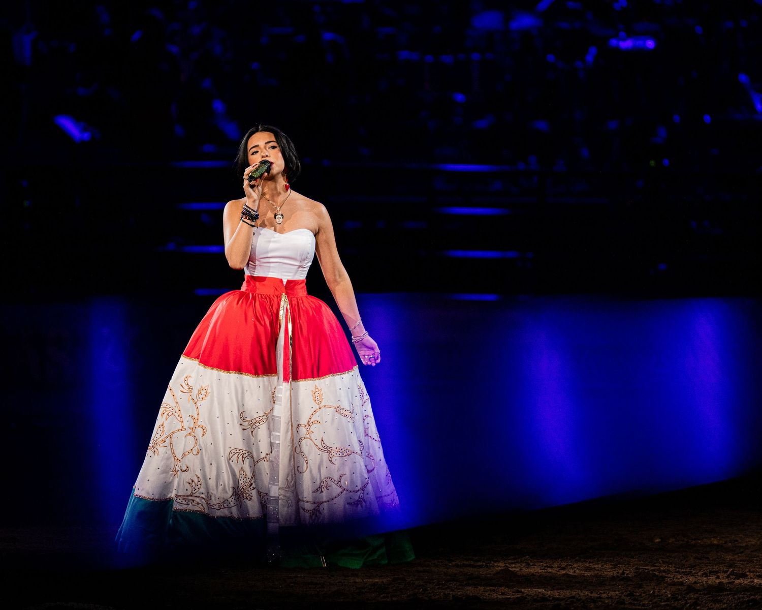 Performer in elegant white and red ball gown singing on illuminated stage.